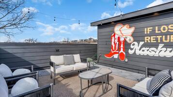An outdoor patio area with a sofa, chairs, and a table. There is a wall with a large logo and text.