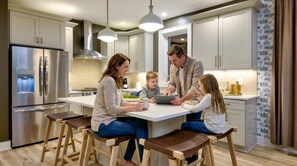 Uma cozinha moderna com eletrodomésticos de aço inoxidável, banquetas de madeira e iluminação pendente.