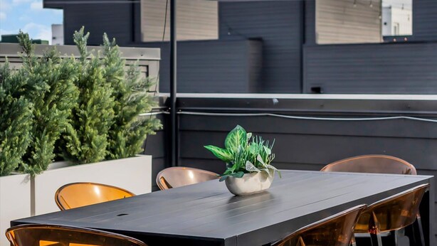 Une terrasse sur le toit, avec une table à manger, des chaises et un pot de fleurs.