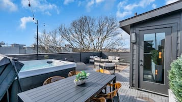 A rooftop patio with a hot tub, outdoor seating, and a glass door entrance.