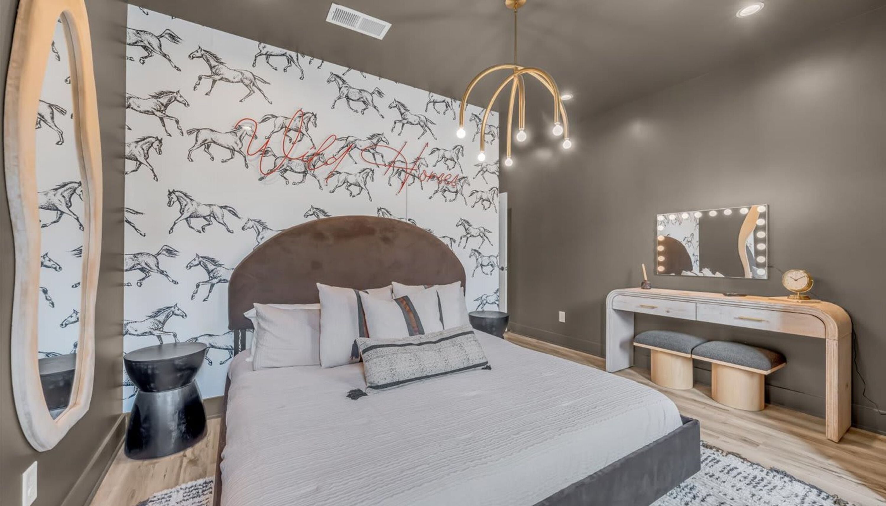 A bedroom with a large bed, a vanity with a mirror, and a wall with a horse pattern.