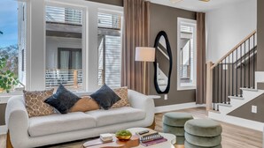 Un salon moderne comprenant un canapé, des poufs, une table basse et un escalier.
