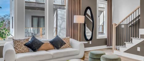 A modern living room with a sofa, ottomans, a coffee table, and a staircase.