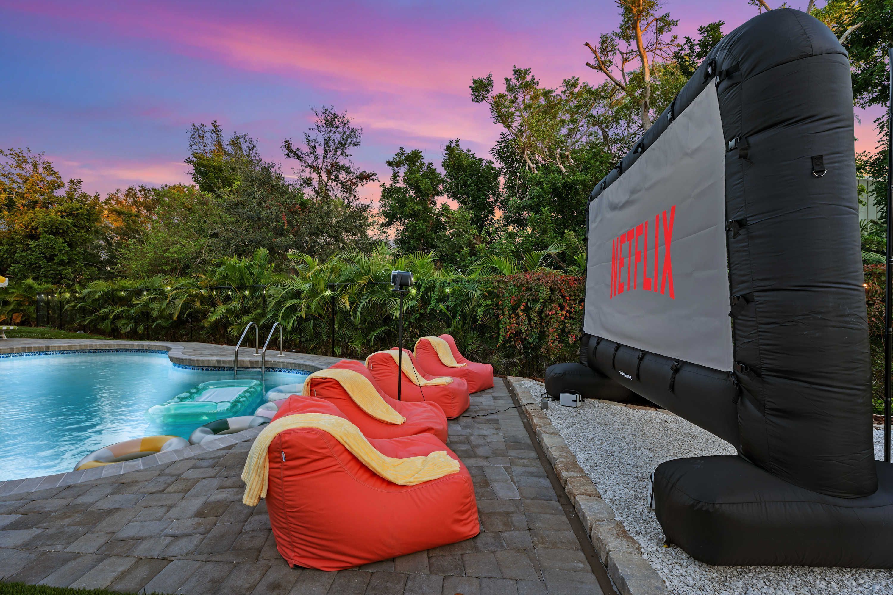 Un espace extérieur avec une piscine, des sièges gonflables et un grand écran gonflable sur lequel est affiché le logo de Netflix.