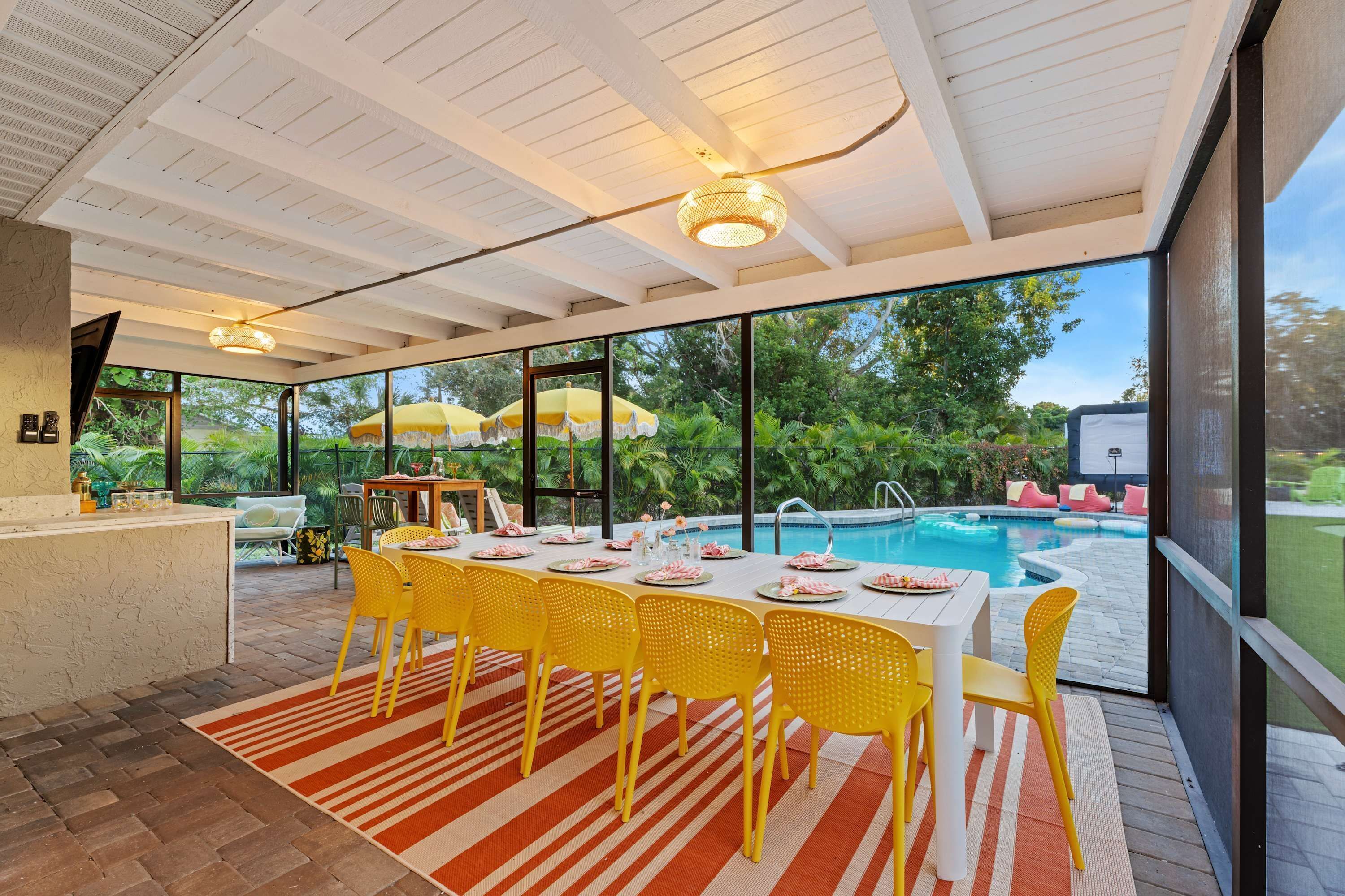 Un coin repas avec vue sur la piscine, comprenant une table dressée pour quatre personnes, des chaises jaunes et un tapis à rayures.
