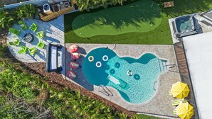 Vista aerea di una zona piscina con idromassaggio, sedie a sdraio e un campo pratica da golf.