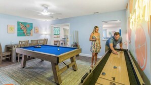 Una stanza con tavolo da biliardo, tavolo da shuffleboard e ventilatore a soffitto.