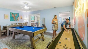 Ein Zimmer mit Billardtisch, Shuffleboard und Deckenventilator.
