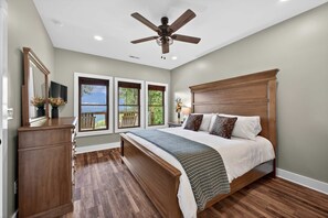 Un dormitorio con una cama grande, un ventilador de techo y vistas al exterior a través de las ventanas.