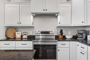 A modern kitchen with white cabinetry, a stainless steel range, and a coffee maker.