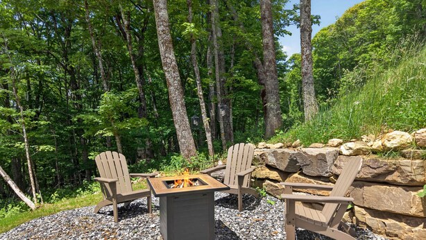 Un espacio al aire libre con sillas Adirondack y un hogar para fuego, rodeado de grava y rocas, en un área boscosa.