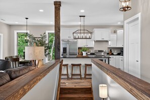 Una cocina moderna con armarios blancos, un refrigerador de acero inoxidable e isla de madera con taburetes de bar.