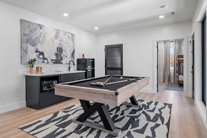 Un espacio moderno con mesa de billar, área de cocina y un cuadro abstracto de gran tamaño.