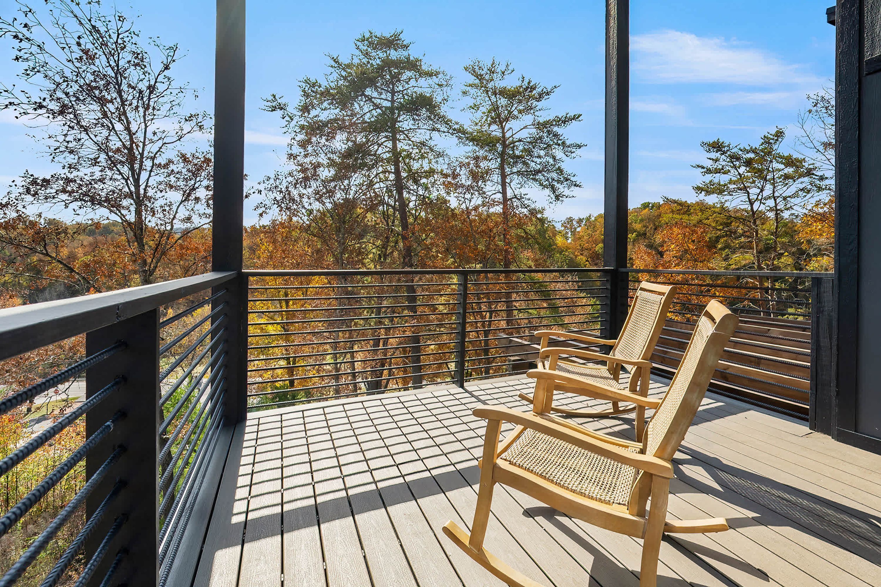 A wooden deck with a metal railing, a wicker rocking chair, and a view of autumn trees.
