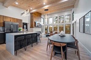 A modern kitchen with a central island, bar stools, and a dining area with a round table and chairs. - Luxury 3 Br Cabin Indoor Pool Hot Tub Fire Pit (Sevierville)