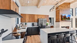 A modern kitchen with a central island, black cabinetry, and a large refrigerator. - Luxury 3 Br Cabin Indoor Pool Hot Tub Fire Pit (Sevierville)