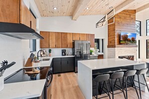 A modern kitchen with a central island, black cabinetry, and a large refrigerator. - Luxury 3 Br Cabin Indoor Pool Hot Tub Fire Pit (Sevierville)