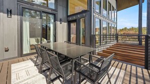 An outdoor dining area with a glass table and metal chairs, overlooking a deck and a scenic view. - Luxury 3 Br Cabin Indoor Pool Hot Tub Fire Pit (Sevierville)