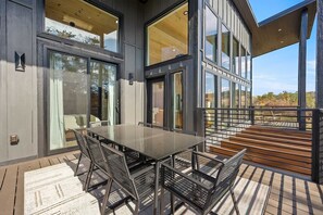 An outdoor dining area with a glass table and metal chairs, overlooking a deck and a scenic view. - Luxury 3 Br Cabin Indoor Pool Hot Tub Fire Pit (Sevierville)