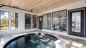 A modern indoor pool area with a wooden ceiling, large windows, and a clear view of the outdoors. - Luxury 3 Br Cabin Indoor Pool Hot Tub Fire Pit (Sevierville)