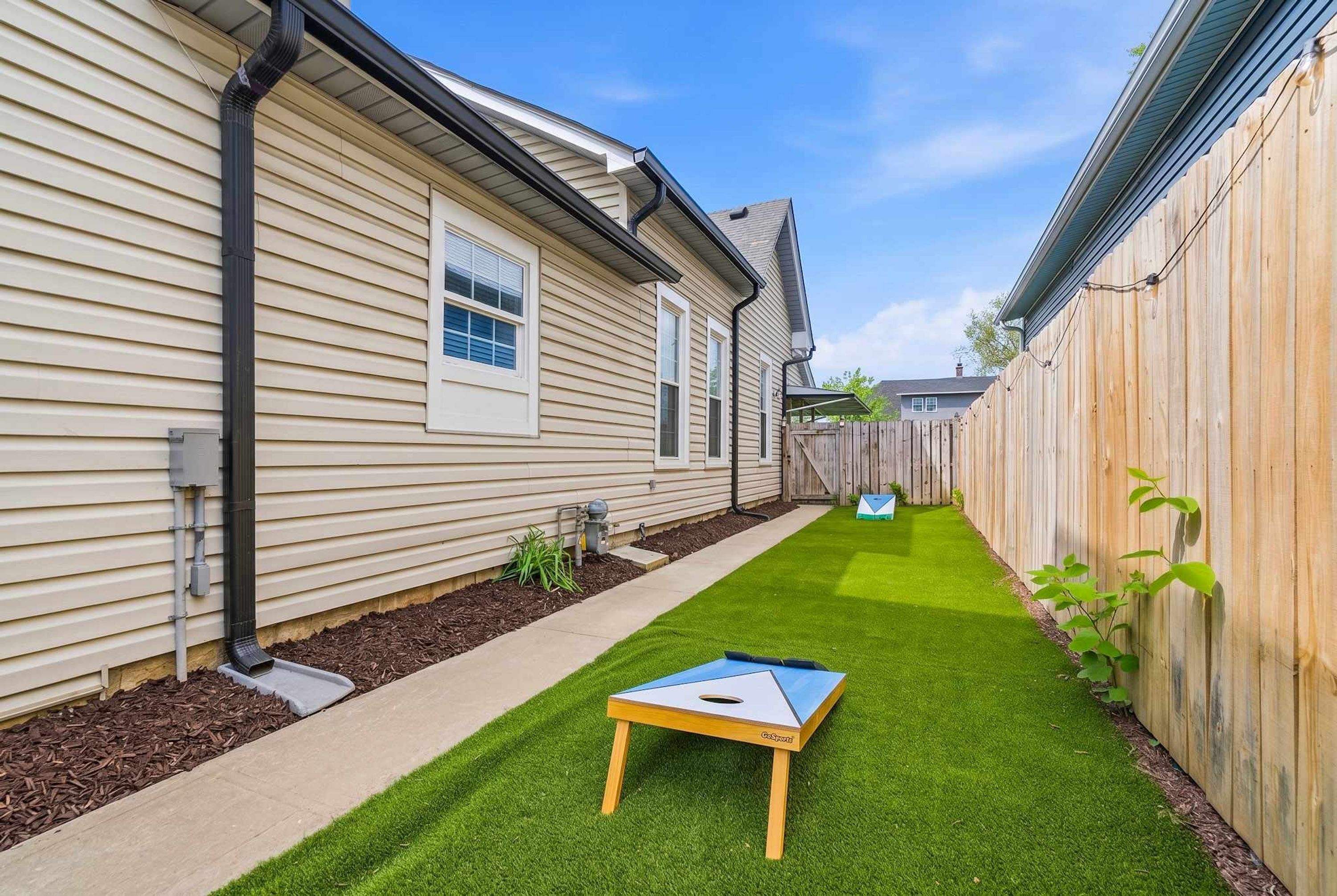Un jardin à l’arrière d’une maison, avec une pelouse, une petite table et une clôture en bois.