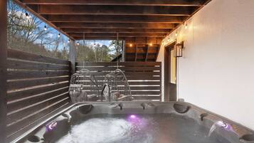 A hot tub with a wooden deck and a view of trees.