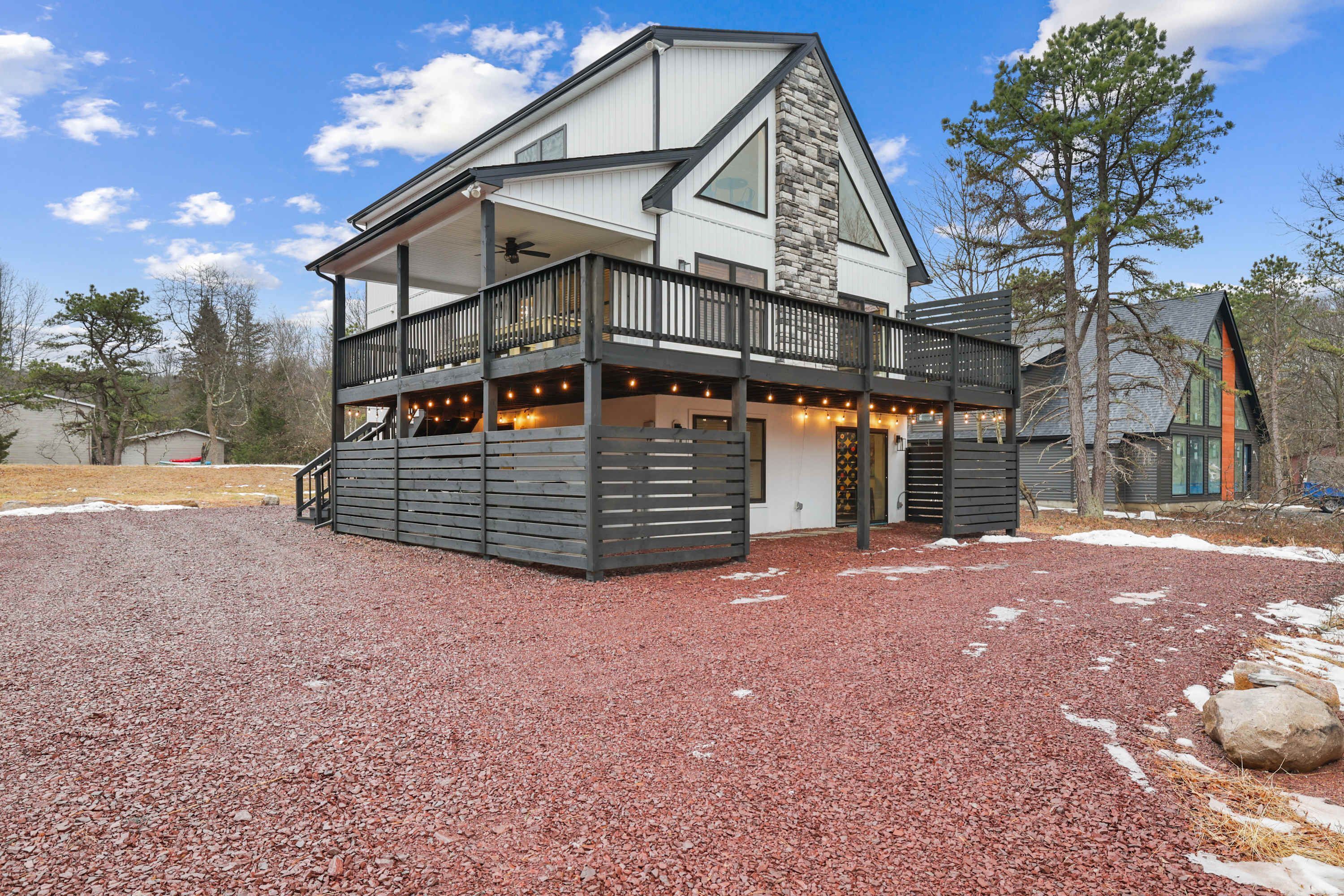 A two-story house with a balcony, a stone facade, and a gravel driveway.