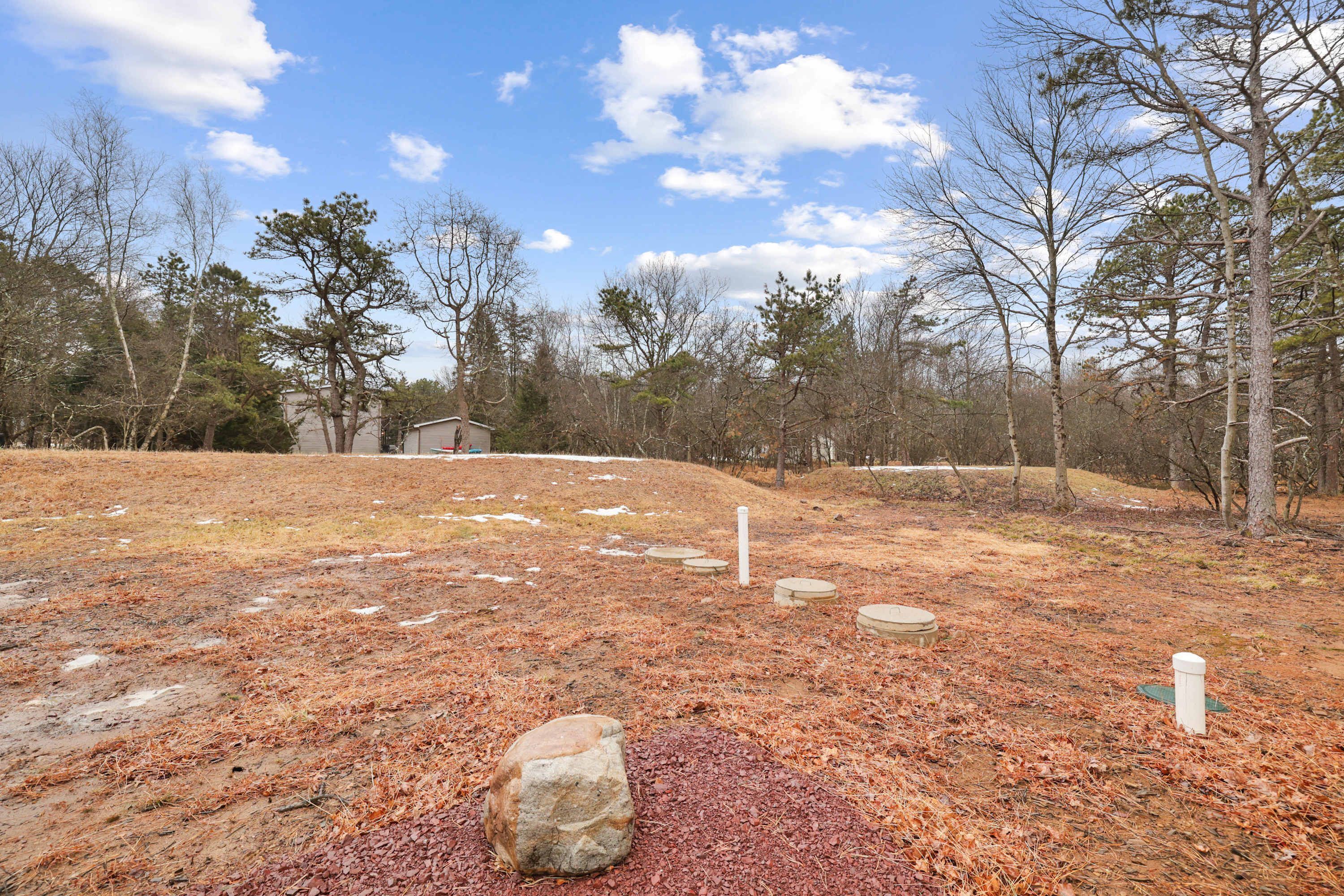 A natural outdoor area with a large rock in the foreground, a small shed in the background, and a clear sky.