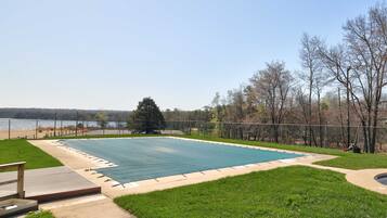 A rectangular swimming pool with a surrounding deck, a grassy area, and a view of a body of water and trees in the background.