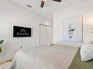 Ein Schlafzimmer mit einem Bett, einem an der Wand montierten Fernseher, einer Tür und einem Gemälde eines Segelboots.