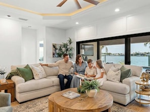 A family sitting on a beige sectional sofa with a view of the water. - Harbor Villa Waterfront Pool Spa Firepit (Indian Rocks Beach)