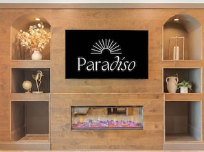Ein an der Wand befestigtes Schild mit dem Wort 'Paradiso' und einem Sonnendesign, seitlich von Regalen mit Dekorationsobjekten eingerahmt.