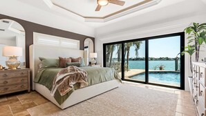 A bedroom with a large bed, a nightstand, a dresser, a ceiling fan, and a view of a pool and ocean. - Harbor Villa Waterfront Pool Spa Firepit (Indian Rocks Beach)