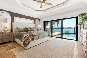 Ein Schlafzimmer mit einem großen Bett, einem Nachttisch, einer Kommode, einem Deckenventilator und Blick auf Pool und Meer.