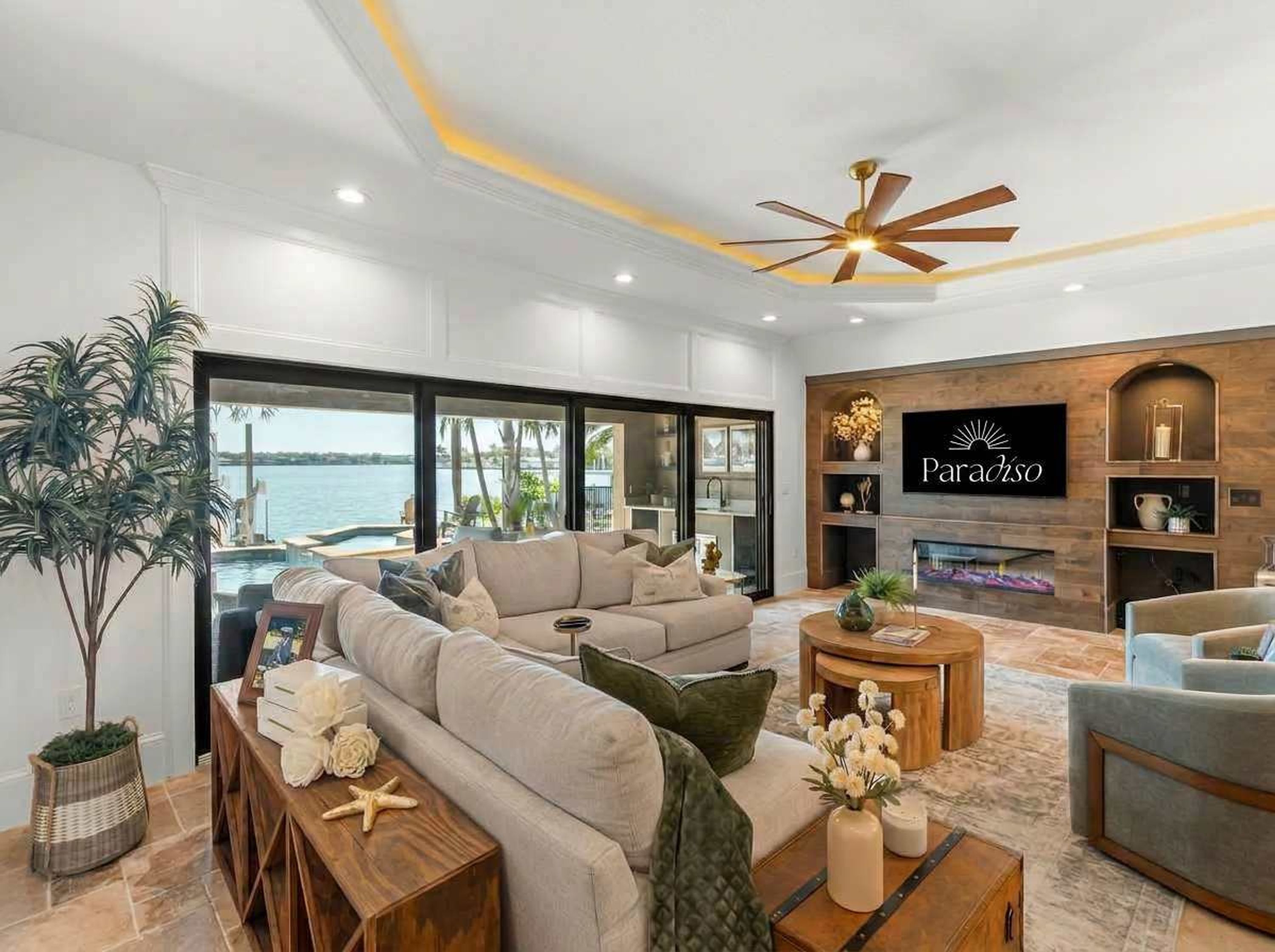 A modern living room with a sofa, coffee table, and a fireplace. There is a large window overlooking a body of water.