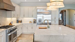 A modern kitchen with white cabinetry, a large island, stainless steel appliances, and a pendant light fixture. - Harbor Villa Waterfront Pool Spa Firepit (Indian Rocks Beach)