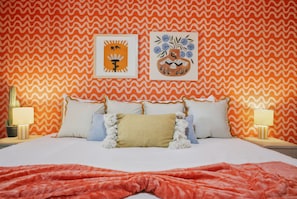 A bed with multiple pillows and a blanket, a wall with a wavy pattern, and two framed artworks. - Drive-in Dream - Theater - Pool - Pickleball (San Antonio)
