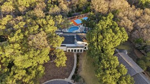 An aerial view of a residential property with a swimming pool, a tennis court, and a large house surrounded by trees. - Drive-in Dream - Theater - Pool - Pickleball (San Antonio)