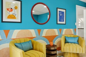 A room with two yellow armchairs, a round mirror, and two framed artworks on a blue wall. - Drive-in Dream - Theater - Pool - Pickleball (San Antonio)