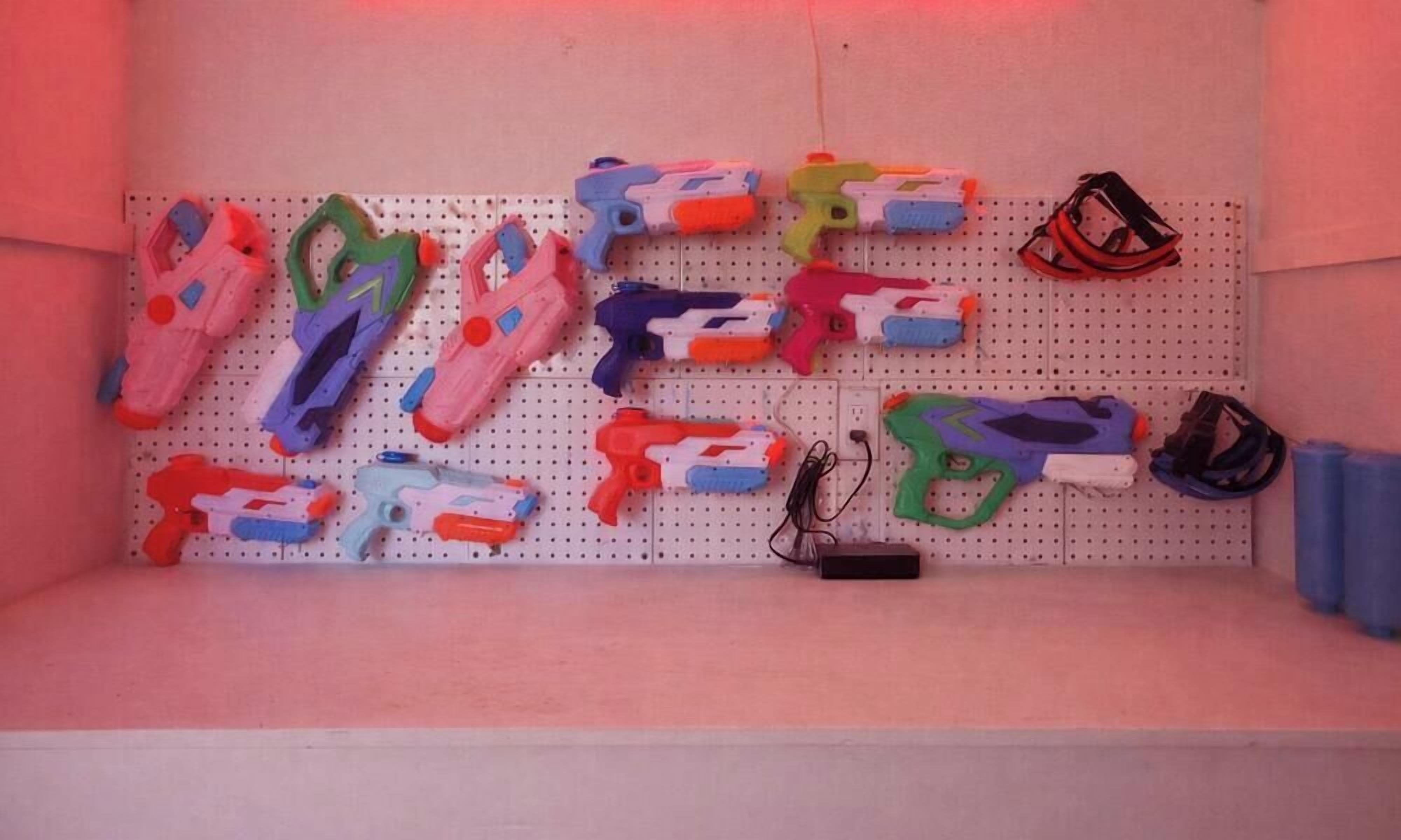 Una pared de tablero perforado con varios juguetes de pistolas de colores y un par de gafas.