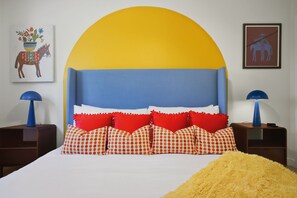 A bedroom with a large bed, a headboard with a yellow and blue color scheme, red and white patterned pillows, and two blue lamps on nightstands. - Drive-in Dream - Theater - Pool - Pickleball (San Antonio)