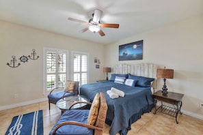 A bedroom with a bed, a chair, a table, a lamp, and a ceiling fan. - Sunrise Beach Villa Beach Views Private Elevator (Port Aransas)