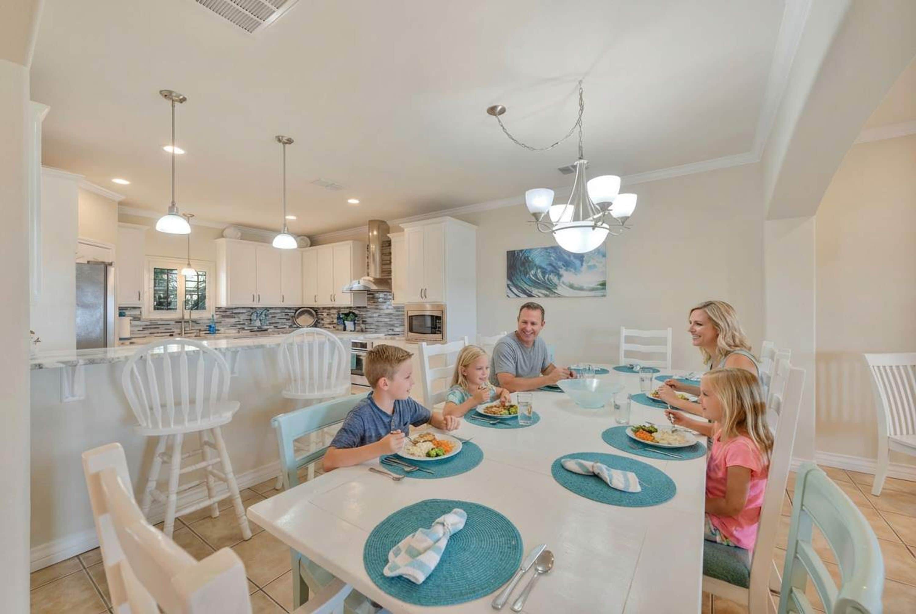 A family dining in a modern kitchen with white cabinetry, a central island, and pendant lighting.