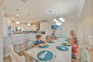 A family dining in a modern kitchen with white cabinetry, a central island, and pendant lighting. - Sunrise Beach Villa Beach Views Private Elevator (Port Aransas)