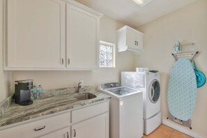 A compact kitchen with a sink, a coffee maker, a washing machine, and a window with blinds. - Sunrise Beach Villa Beach Views Private Elevator (Port Aransas)