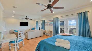 Habitación de hotel con cama, escritorio, silla, ventilador de techo y televisor.