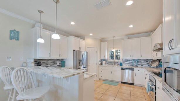 A kitchen with white cabinets, a central island with bar stools, a refrigerator, and a dishwasher. - Sunrise Beach Villa Beach Views Private Elevator (Port Aransas)