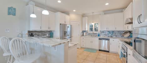 A kitchen with white cabinets, a central island with bar stools, a refrigerator, and a dishwasher.
