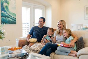 A family sitting on a couch with a bowl of popcorn and a remote control, in a room with a painting on the wall. - Sunrise Beach Villa Beach Views Private Elevator (Port Aransas)