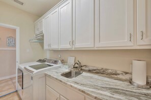 A kitchen with white cabinets, a washing machine, a sink, and a marble countertop. - Sunrise Beach Villa Beach Views Private Elevator (Port Aransas)